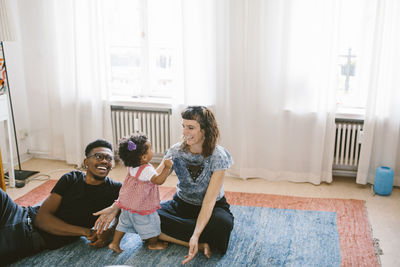 Happy mother and father with daughter on carpet at home