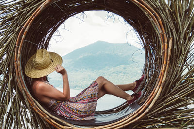 Woman wearing hat while sitting on wicker basket