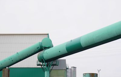 Low angle view of green pipes in factory against clear sky