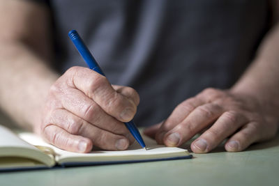 Hands of a pensioner working at the table writes with a pen in a notebook