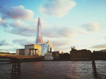 View of city at waterfront against cloudy sky