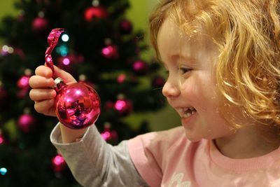 Close-up of cheerful girl holding pink christmas ornament