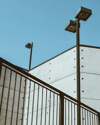 Low angle view of metallic structure against wall against clear blue sky