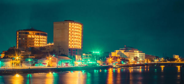 Illuminated buildings by river in city at night