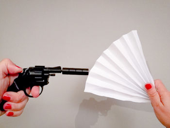 Cropped hand holding handgun and paper fan against wall