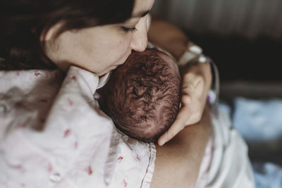 Mid view of mother in hospital bed kissing newborn son's head