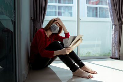 Woman sitting on book against window