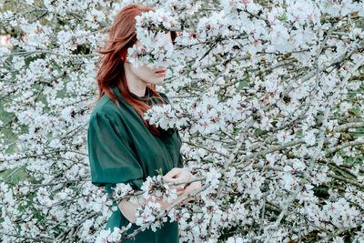 Portrait of young woman standing against tree