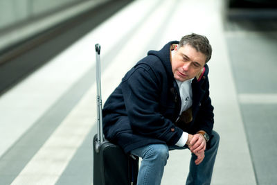 Man sitting on luggage at railroad station platform