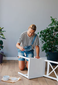 Portrait of young woman using digital tablet while sitting against wall