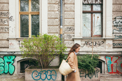 Side view of young woman walking by building with graffiti text