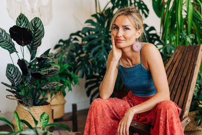 Attractive thirties woman sitting on an armchair against the background of plants