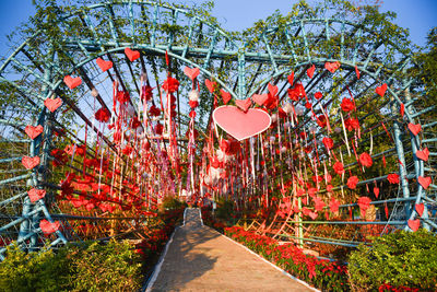 View of red heart shape on footpath by plants against sky