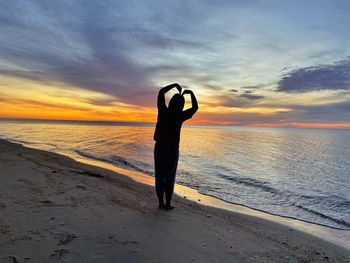 Rear view of man standing at beach against sky during sunset
