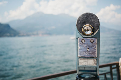 Close-up of coin-operated binoculars by sea against sky