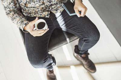 High angle view of man holding coffee cup and note pad at home office