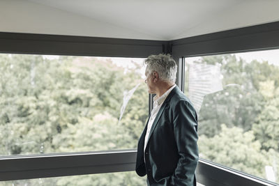 Businessman looking though window while standing at office