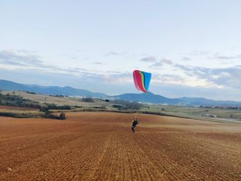 Person paragliding over field against sky