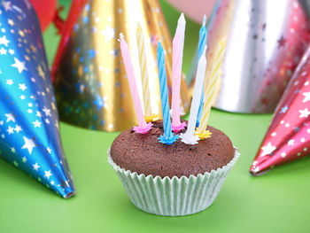 Chocolate muffin decorated with eight candles with party cone caps in the background