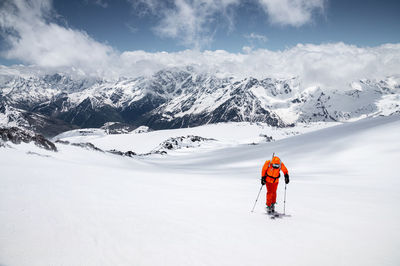 Young male freerider guide in a yellow ski suit with a backpack on his shoulders climbing mountain 