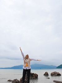 Portrait of woman with arms outstretched standing against sea