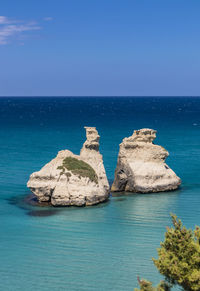 Rocks in sea against clear blue sky