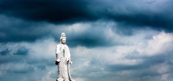 Low angle view buddha statue against storm clouds 