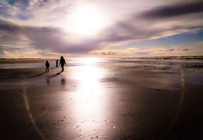 Silhouette people on beach against sky during sunset