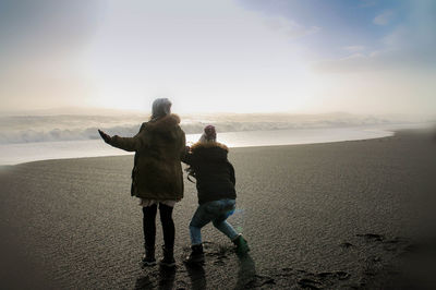 Rear view of women standing on beach against sky