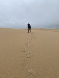 Rear view of man walking on sand at beach against sky