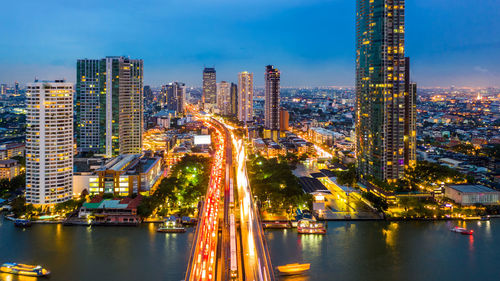 Illuminated buildings by river against sky at night