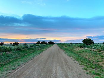 Dirt road amidst field against sky