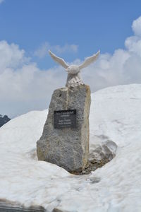 Cross on rock against sky during winter