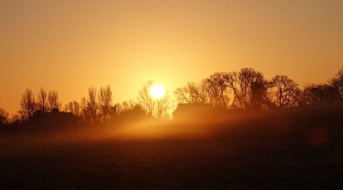 Silhouette trees on field against sky during sunset