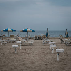 Lounge chairs and parasols on beach against sky