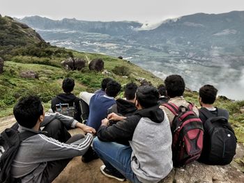 Rear view of men with backpacks sitting on mountain