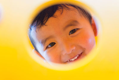 Portrait of cute smiling boy looking through hole in yellow playground equipment