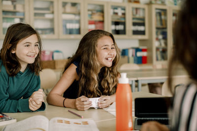 Smiling female student with paper sitting by friend in classroom