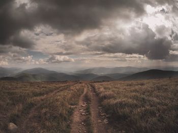 Dirt road on field against sky