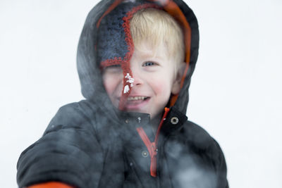Close-up portrait of boy smiling on field during snowfall