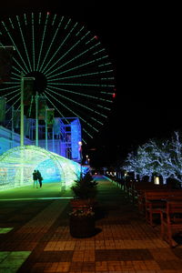 Illuminated ferris wheel against buildings in city at night