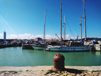 Sailboats moored at harbor against blue sky