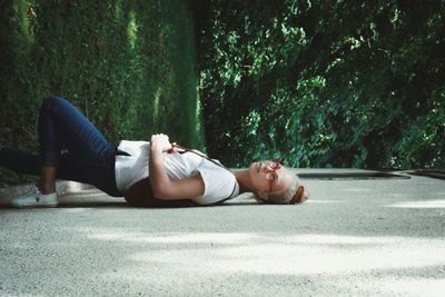 Tilt image of woman leaning on wall against trees