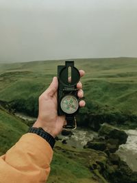 Cropped hand holding navigational compass against landscape