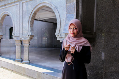 Portrait of woman in hijab holding counting rosary beads while praying at mosque