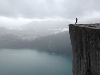 Distant view of man standing at preikestolen against cloudy sky