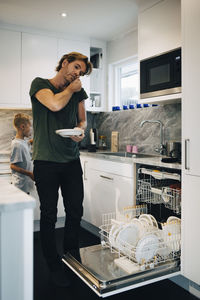 Man talking on mobile phone while using dishwasher at kitchen