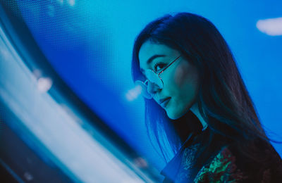 Close-up of young woman standing against illuminated city at night