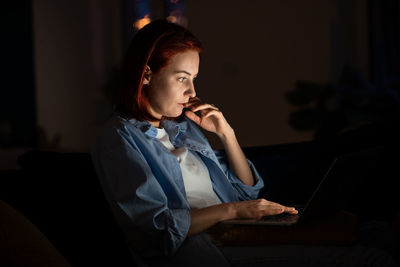 Focused freelancer woman looking laptop screen at night working from home.