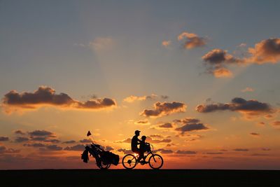 Silhouette of man with child riding bicycle on field against orange sky